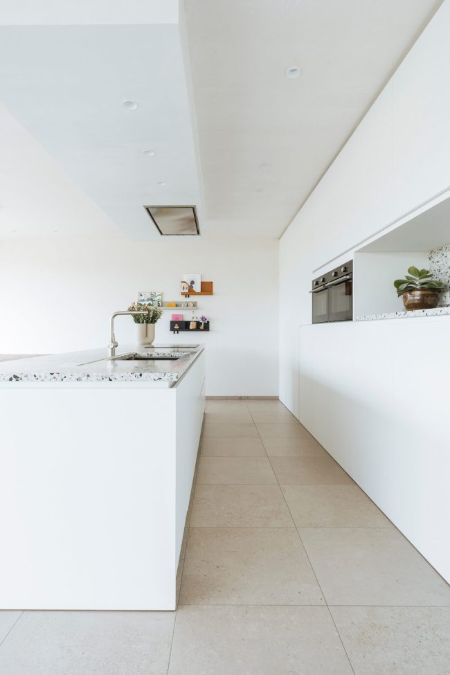 Scandinavische keuken met wit eiland, terrazzo werkblad en witte kastenwand in Ardooie, Kaster Keukens