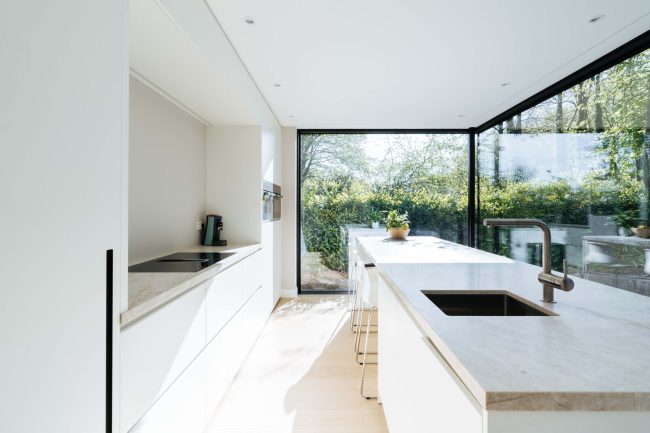 Scandinavische keuken met witte fronten, licht natuurstenen werkblad en tuinzicht in Brugge, Kaster Keukens