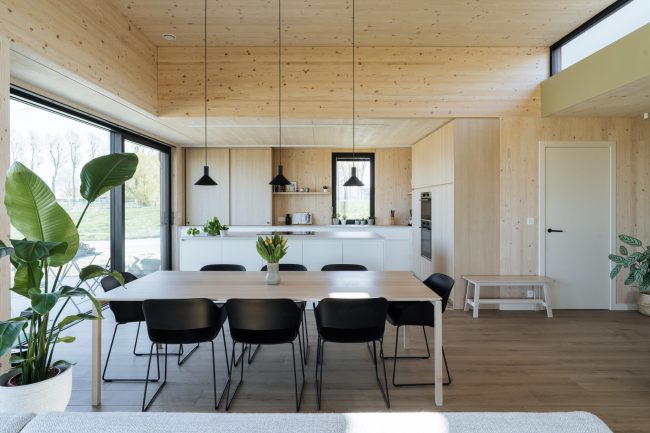 Scandinavische keuken met houten wanden en plafond, wit eiland en eettafel met zwarte stoelen in Deerlijk, Kaster Keukens