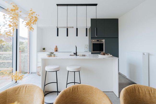 Scandinavische keuken met wit eiland, donkergroene hoge kasten en zwarte hanglampen in Kortrijk, Kaster Keukens