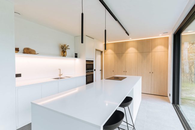 Scandinavische keuken met wit eiland, eiken kastenwand en zwarte hanglampen in Roeselare, Kaster Keukens