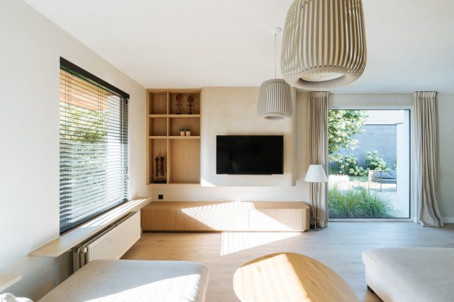 Tv-meubel op maat in lichte eikenlook met afgeronde hoek en open vakkenkast naast een beige tv-wand, Kaster Keukens.
