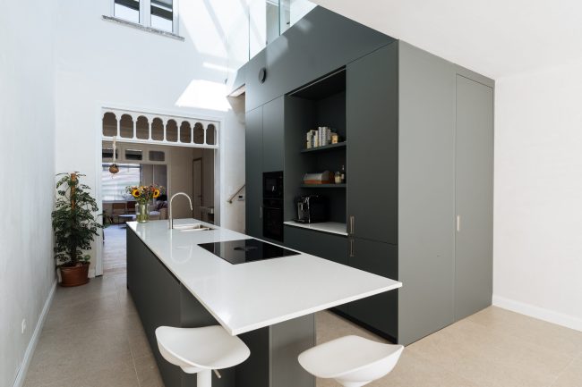 Moderne keuken met donkergroene fronten, wit werkblad, lang kookeiland met zitplaatsen en een open koffienis, Kaster Keukens.